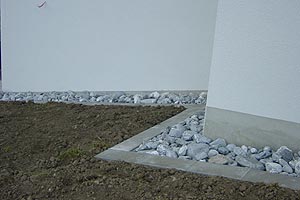 Rusch Erdbewegungen GmbH - Umgebungen - Fassadenschutz mit Bollensteinen und Rasenabgrenzung mit Gartenplatten 